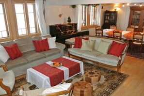 A cozy living room with a sofa, armchairs, a dining table, and a piano.