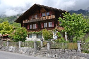A wooden chalet with a stone foundation, multiple windows, and a balcony.