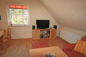 Ein Zimmer mit Fernseher, Holzmöbeln, Heizkörper und einem Fenster mit Jalousien.