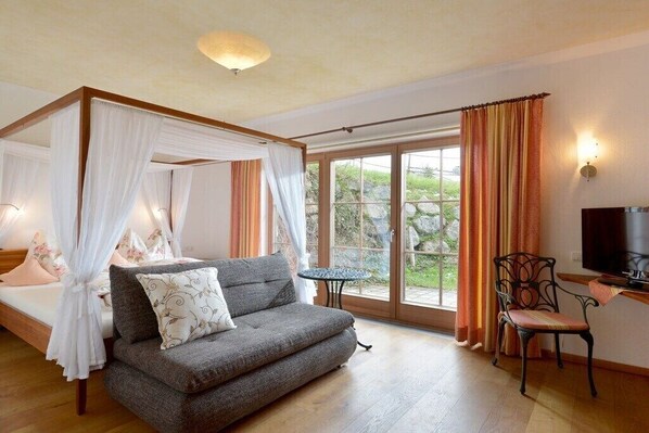 A bedroom with a four-poster bed, a sofa, a TV, and a chair.
