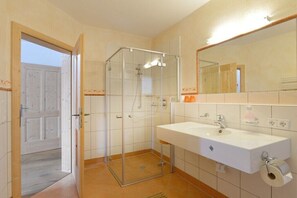 A bathroom with a glass-enclosed shower, a white sink, a mirror, and a door leading to another room.