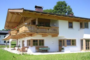 A two-story house with a balcony, a wooden porch, and a small garden area.