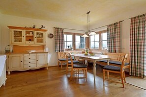 Un coin repas avec une table en bois, des chaises, un buffet et des rideaux à carreaux.