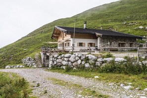 Un chalet de montagne à la façade en pierre, doté d’un balcon en bois et offrant une vue sur les collines environnantes.