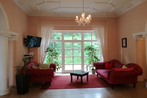 Ein Zimmer mit zwei roten Sofas, einem schwarzen Couchtisch, einem Fernseher und einem großen Fenster mit Vorhängen.