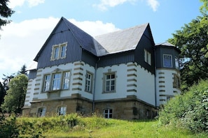 Ein großes, historisches Gebäude mit einem markanten Eckturm, zahlreichen Fenstern und einem Steinfundament.