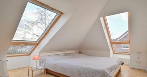 Ein Schlafzimmer mit schrägverdeckelter Decke, Dachfenstern, einem Bett, einem Nachttisch und einer Lampe.