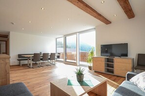 A modern living room with a dining area, a flat-screen TV, and large windows. - 100 m² Guesthouse Sonne (Bichlbach)
