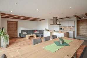 A modern living room with a sofa, dining table, and kitchen area. - 100 m² Guesthouse Sonne (Bichlbach)