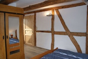Ein Schlafzimmer mit freiliegenden Holzbalken, einem Bett mit blauen und weißen Kissen und einer Bettdecke, einem Holzschrank und einer Tür zu einem anderen Raum.