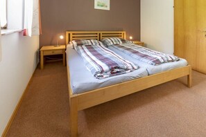 Ein Doppelbett mit kariertem Überwurf, zwei Nachttische, ein Beistelltisch, eine Wandlampe und eine Tür.