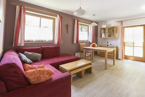 Ein gemütliches Wohnzimmer mit einem roten Sofa, einem Holztisch und einem Essbereich mit Tisch und Stühlen.
