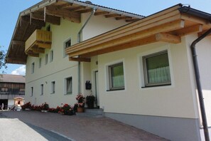 A multi-story building with a wooden balcony, a covered entrance, and a paved driveway. - Holiday apartment with 1 bedroom (Piesendorf)