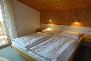 A double bed with two pillows, a wooden headboard, bedside tables, and a window with curtains. - Holiday apartment with 1 bedroom (Piesendorf)