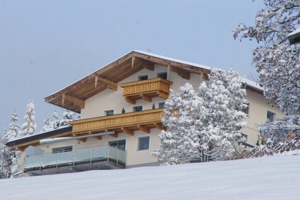 A multi-story building with a wooden balcony, surrounded by snow-covered trees. - Holiday apartment with 1 bedroom (Piesendorf)