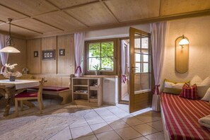 Ein gemütliches Zimmer mit Holzbalkendecke, einem Bett mit gestreifter Bettdecke, einem Tisch mit Stühlen und einem Fenster mit Vorhängen.