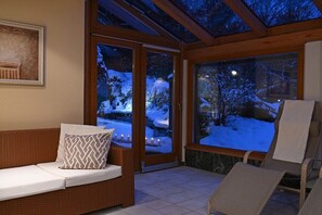 Ein Zimmer mit einer Couch, einem Sessel und einer Glastür, die zu einem verschneiten Außenbereich führt.