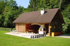 Ein Holzgebäude mit geneigtem Dach, einem Schild mit der Aufschrift 'GRILLHUTTE' und einem Schachbrett davor.