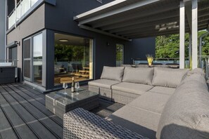 Ein moderner Außenbereich mit einer Sitzecke, einer Glastür, die auf eine Terrasse führt, und einem Tisch mit Glasplatte.