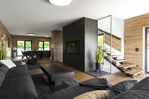 A modern living room with a sofa, coffee table, TV, staircase, and dining area. - Holiday home with 3 bedrooms (Neukieritzsch \/ OT Kahnsdorf)