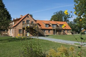 Ein großes Backsteingebäude mit geneigtem Dach, zahlreichen Fenstern und einer zentralen Treppe, die zu einem Balkon führt.