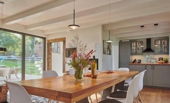 A dining area with a wooden table, chairs, a vase with flowers, and a kitchen in the background. - Holiday home with 4 bedrooms (Friederikenhof)