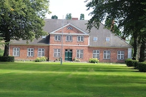 A large brick building with a symmetrical facade, a central entrance with a green door, and a well-maintained lawn in front. - Holiday home with 4 bedrooms (Friederikenhof)