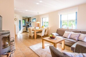 Ein gemütliches Wohnzimmer mit einer Couch, einem Esstisch mit Stühlen, einem Kamin und einer Küche im Hintergrund.