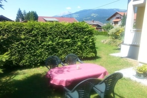 Eine Terrasse mit Tisch und Stühlen, umgeben von Grünpflanzen und Blick auf die Berge.