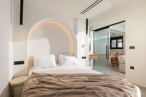 Quarto moderno com teto arredondado, cama com roupa de cama branca, janela grande e porta de vidro que dá para uma sala de jantar.