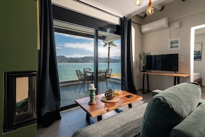Uma sala de estar moderna com uma grande porta de vidro deslizante que dá para uma varanda com vista para o mar e as montanhas.