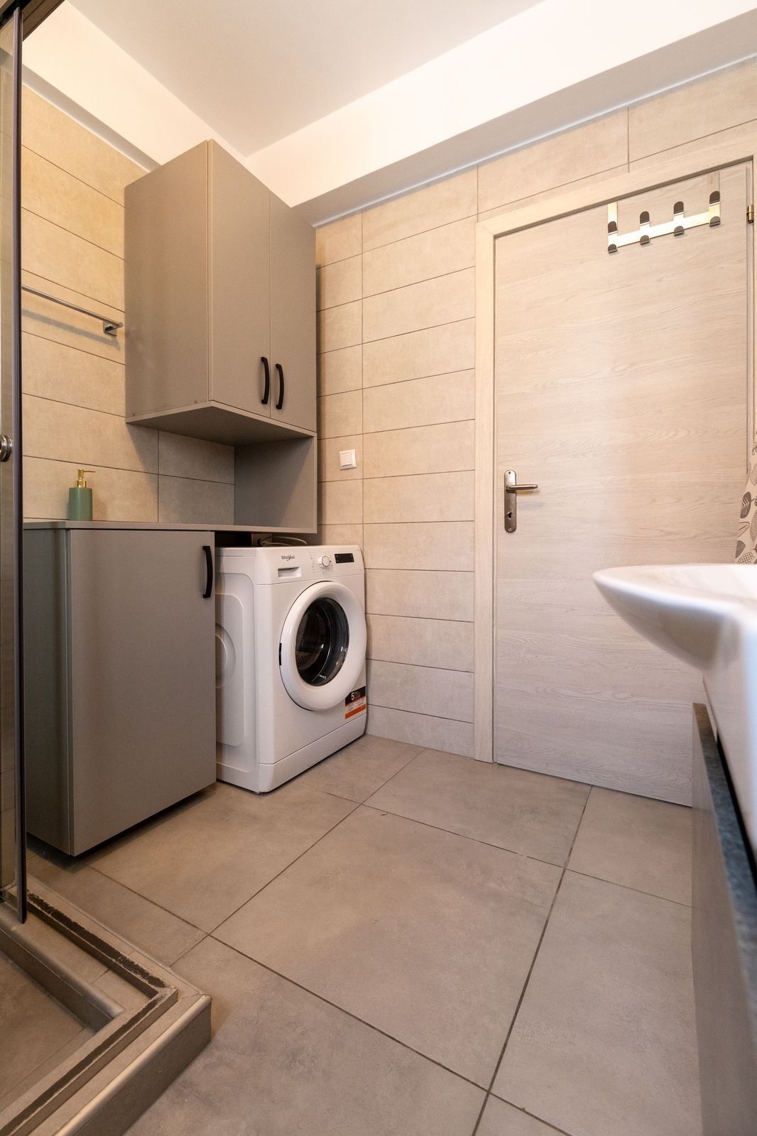 A compact kitchen with a washing machine, cabinets, and a door with a handle.