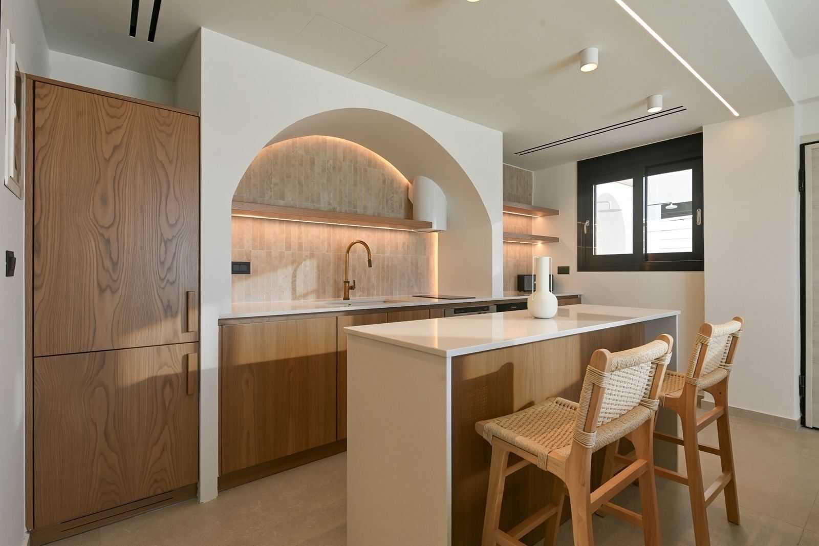 A modern kitchen with wooden cabinetry, an island with bar stools, and a window providing natural light.