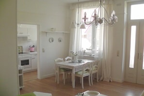Ein Essbereich mit Tisch, Stühlen, einer Chandelierleuchtre und einem Fenster mit Vorhängen.
