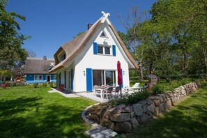 Ein Haus mit steilem Dach, einer Steinwand und einer Terrasse mit Gartenmöbeln.