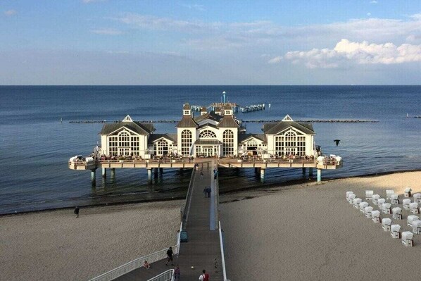 Eine Pier, die zu einem Gebäude mit mehreren Fenstern und einem Balkon führt, das sich über ein Gewässer erstreckt.
