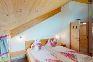 Ein Schlafzimmer mit Holzboden, einem Bett mit floralem Bettzeug, einem Nachttisch und einem Kleiderschrank.
