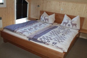 A wooden bed with two pillows, a blanket, and a bedspread with deer and floral patterns.
