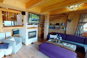 Ein gemütliches Holzhaus-Interieur mit Kamin, Fernseher, Sofa und Bücherregal.