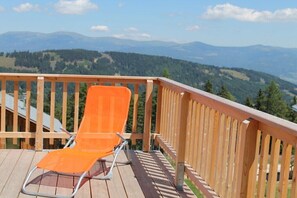 Eine Holzterrasse mit einem einzelnen orangefarbenen Stuhl, mit Blick auf eine gebirgige Landschaft.