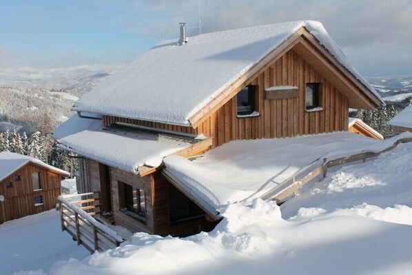 Eine Holzhütte mit geneigtem Dach, umgeben von verschneiter Landschaft.