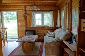 A cozy cabin interior with a wooden ceiling, a sofa, a table, a television, and a window with curtains. - Holiday home in Altwarp with swimming pool (Altwarp)