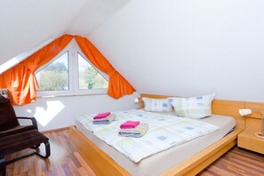 Ein Schlafzimmer mit einem Hochbett, einem Sessel, einem Nachttisch mit Lampe und einem Fenster mit Vorhängen.