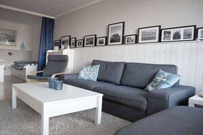 Ein Wohnzimmer mit grauem Sofa, einem weißen Couchtisch, einem blau gemusterten Kissen, einem grauen Sessel und einer Wand mit gerahmten Bildern.