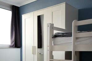 Ein Etagenbett mit weißem Gestell, ein Bett darüber, ein weißer Kleiderschrank und ein Fenster mit Vorhängen.