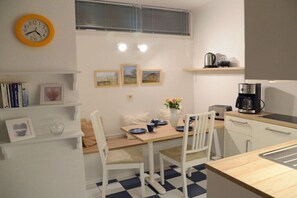 Eine kleine Küche mit Esstisch, Stühlen, einer Kaffeemaschine und einer Uhr an der Wand.