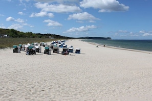 A beach with rows of beach chairs and umbrellas, a sandy shore, and a calm sea. - Beach House Deichkrone (Baabe)