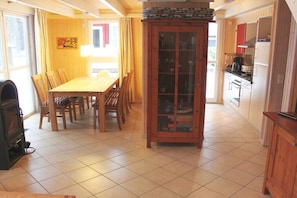 A dining area with a wooden table and chairs, a cabinet with glass doors, and a kitchen area with cabinets and appliances. - Beach House Deichkrone (Baabe)