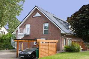 Ein zweistöckiges Haus mit Backsteinfassade, einem überdachten Carport und einer Treppe, die zum Obergeschoss führt.