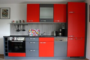 Eine Küche mit roten und grauen Schränken, einem Herd, einem Backofen und einer Kaffeemaschine.